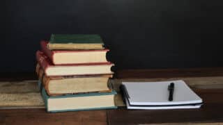 Stack of old books next to notebook and pen