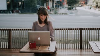 Woman working on MacBook at table on coffee shop patio